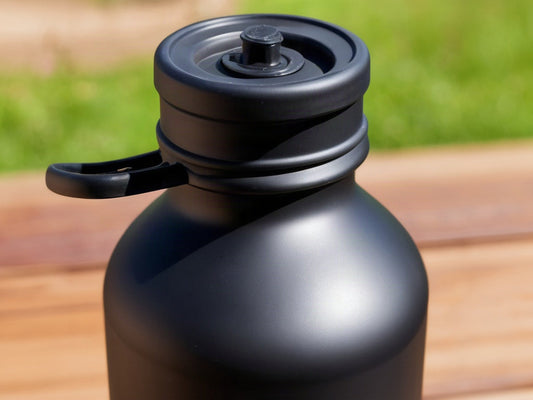 A cropped close-up of a black twist loop chug bottle lid held by its carry loop against a blurred green outdoor background