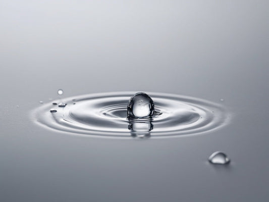 Close-up of a clean water droplet creating ripples on a smooth surface
