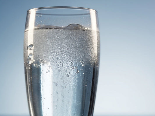 A macro close-up of a clear glass of sparkling water with rising bubbles and condensation in daylight