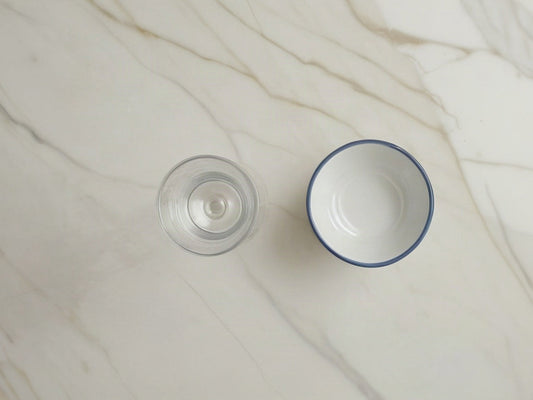 Overhead view of a tall glass of water and a small white ceramic dish on a light marble countertop