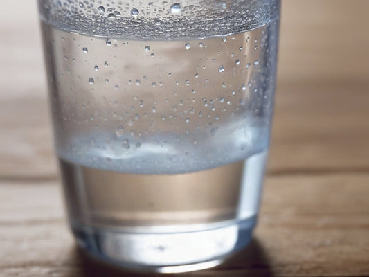 A cold glass of water with condensation droplets beading on the outside on a wooden surface