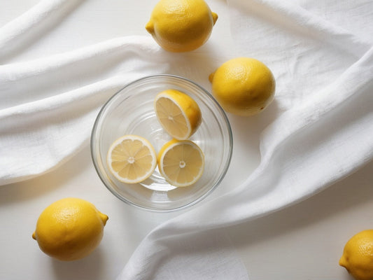 Lemon halves and a glass bowl of water on a white cloth — natural descaling ingredients