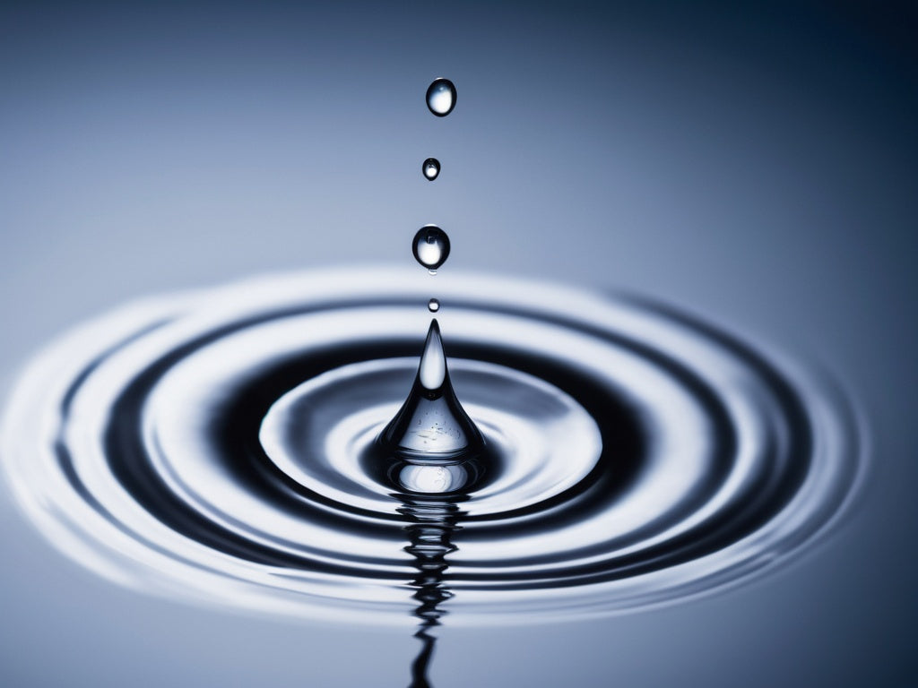 A single water droplet creating concentric ripples in blue-toned water