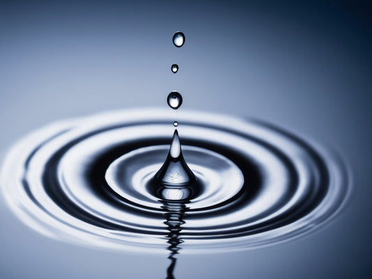A single water droplet creating concentric ripples in blue-toned water