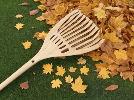 Wooden leaf rake resting beside a pile of golden autumn leaves on a green lawn