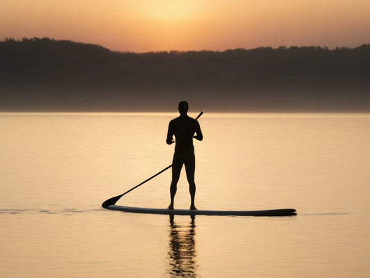 Silhouette of a person stand-up paddleboarding at sunrise