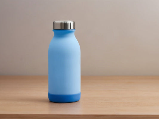 A light blue insulated water bottle with a darker blue silicone protective boot on its base, on a wooden surface in soft daylight