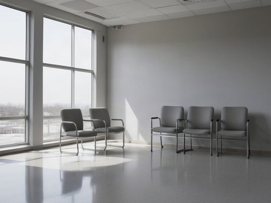 An empty waiting area with plain gray chairs beside a tall window in soft morning light